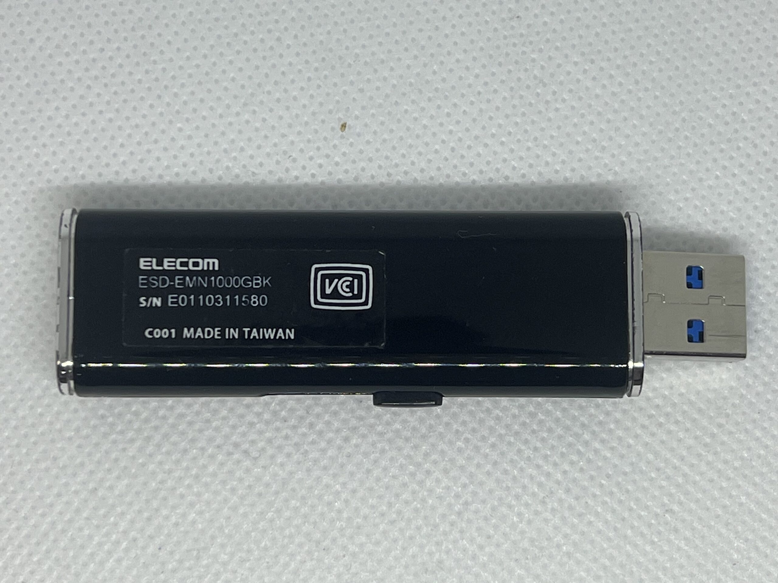 Black Elecom USB dongle labeled ESD-EMN1000GBK with serial E0110311580 and Made in Taiwan, connected to a USB connector visible on the right.